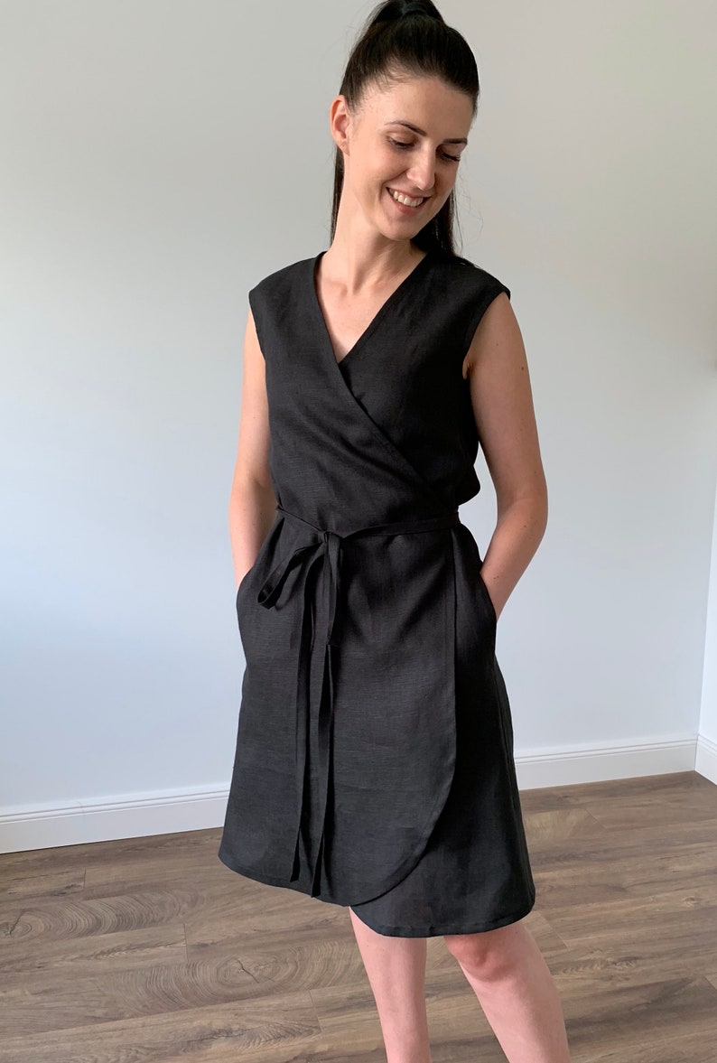 May include: A black linen wrap dress with a V-neckline and short sleeves. The dress has a tie belt and pockets.