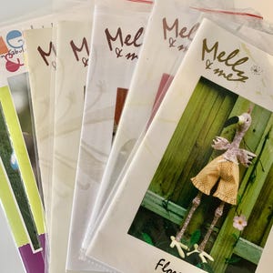 May include: A selection of craft pattern packets in clear plastic sleeves. The packets display the text "Mel & me" in a handwritten style. One packet shows a flamingo doll with yellow shorts. Other packets have the text "fun & fabul".