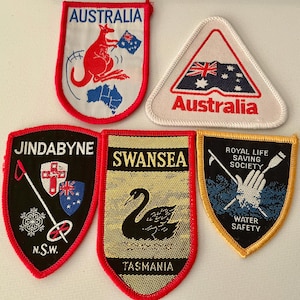 May include: Five embroidered patches featuring Australian themes. One shows a kangaroo and map, another a triangular flag, one for Jindabyne with a ski pole, one for Swansea with a black swan, and one for the Royal Life Saving Society.