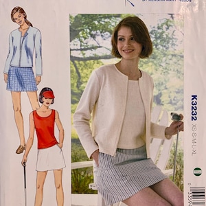 Op de afbeelding: Een naaipatroonpakket met een vrouw in een crèmekleurig jasje en een gestreepte rok, die een golfclub vasthoudt. Het pakket bevat outfit-illustraties en de tekst "KWIK SEW" en "K3232".