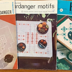 May include: Three vintage instructional craft booklets titled Modern Hardanger, Coloured Hardanger Motifs, and Hardanger For Today. The covers feature photography of embroidered white linens with geometric patterns, displayed with various table settings.