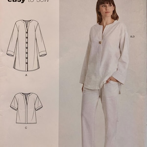 May include: Simplicity sewing pattern S9113 for an easy-to-sew top and trousers set. The pattern includes technical line drawings for a long-sleeve button-front tunic and a short-sleeve version, alongside a photograph of the finished off-white outfit.