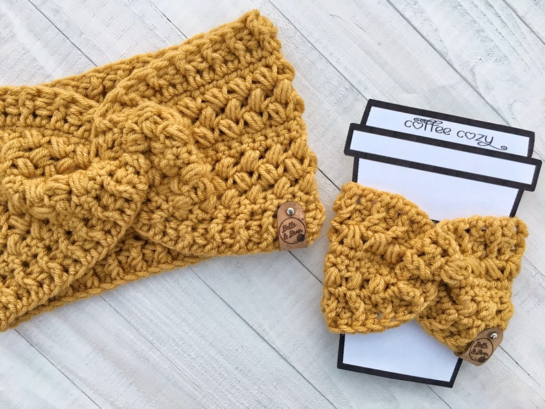 May include: A set of two crocheted items in a mustard yellow color. The larger item is a headband and the smaller item is a coffee cozy. Both items have a knotted design and feature a small brown leather tag with the text "Belle & Bloom".
