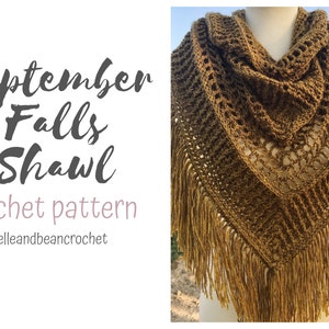 May include: A crocheted shawl with a brown and beige color gradient. The shawl has a lacy pattern and a fringe border. The text "September Falls Shawl crochet pattern @belleandbeancrochet" is visible in the image.