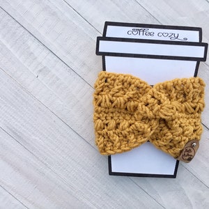 May include: A mustard yellow crocheted coffee cozy with a brown leather tag that says "Little Stitchin'" and a paper coffee cup cutout that says "coffee cozy".