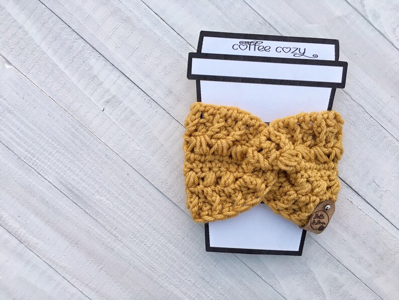 May include: A mustard yellow crocheted coffee cozy with a brown leather tag that says "Little Stitchin'" and a paper coffee cup cutout that says "coffee cozy".
