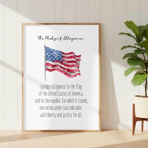 Può includere: Una stampa da parete incorniciata con il testo The Pledge of Allegiance in alto, un'illustrazione ad acquerello di una bandiera americana che sventola al centro e il testo completo del giuramento di fedeltà stampato in nero sotto.