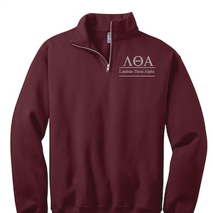 Puede incluir: Una sudadera de color burdeos con cremallera de 1/4 con las letras griegas "ΛΘΑ" y las palabras "Lambda Theta Alpha" bordadas en el pecho.