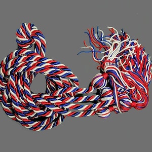 May include: Red, white, and blue graduation tassel with a braided cord and a tassel with multiple strands.