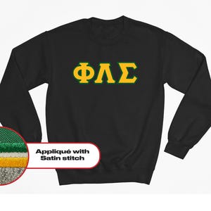 May include: Black sweatshirt with a gold Greek letter fraternity logo "ΦΛΣ" in a green outline. The logo is stitched with a satin stitch.