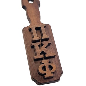 May include: A wooden paddle with the Greek letters IIKP engraved on it. The paddle is brown and has a handle.
