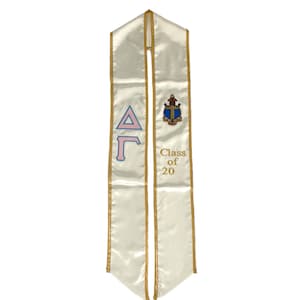 Peut inclure: Une écharpe de graduation blanche avec des bordures dorées et un symbole de sororité Delta Gamma rose et bleu. L'écharpe comporte également un blason doré et le texte "Class of 20".