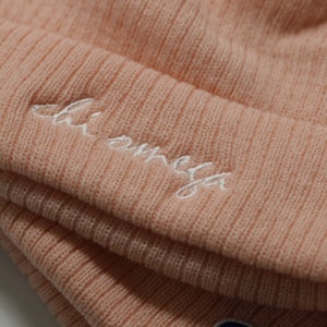 May include: A pink knit beanie with a white embroidered logo that says "Champion" and a small blue and red Champion logo.