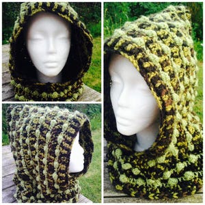 Peut inclure: Une cagoule en crochet aux tons de vert et de brun. La cagoule est réalisée avec un point texturé qui crée une surface bosselée.