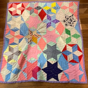 May include: A colorful patchwork quilt with a variety of star patterns in shades of pink, blue, red, yellow, and green. The quilt is bordered with a lavender fabric and is made of various patterned fabrics.