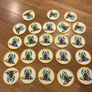 May include: A collection of embroidered patches with a circular design. Each patch features a white background with a yellow border. The central design includes a crescent moon, star, and stylized elements in green, red, and yellow.