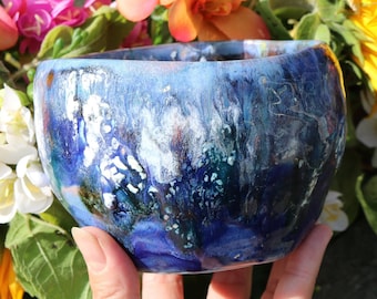 May include: A blue ceramic bowl with white and green swirls and speckles. The bowl is hand-painted and has a unique, abstract design.