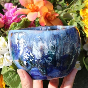 May include: A blue ceramic bowl with white and green swirls and speckles. The bowl is hand-painted and has a unique, abstract design.