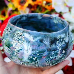 May include: A blue ceramic bowl with a white and green speckled glaze. The bowl has a rounded shape and a wide rim.