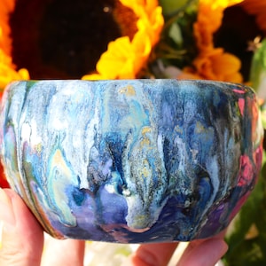 May include: A blue, white and gold ceramic bowl with a swirled, abstract design. The bowl is hand-painted and has a unique, artistic look.