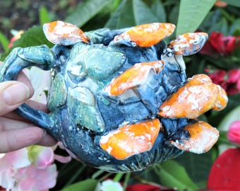 May include: A blue and green ceramic mug with a handle, decorated with orange and white mushrooms. The mug is hand-painted and has a unique, whimsical design.