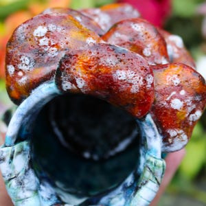 May include: A ceramic vessel with a textured, organic design. The exterior features a blend of reddish-brown and orange hues with white speckles. The interior is a deep blue, with hints of turquoise and white along the rim. The vessel has a unique, artistic appearance.