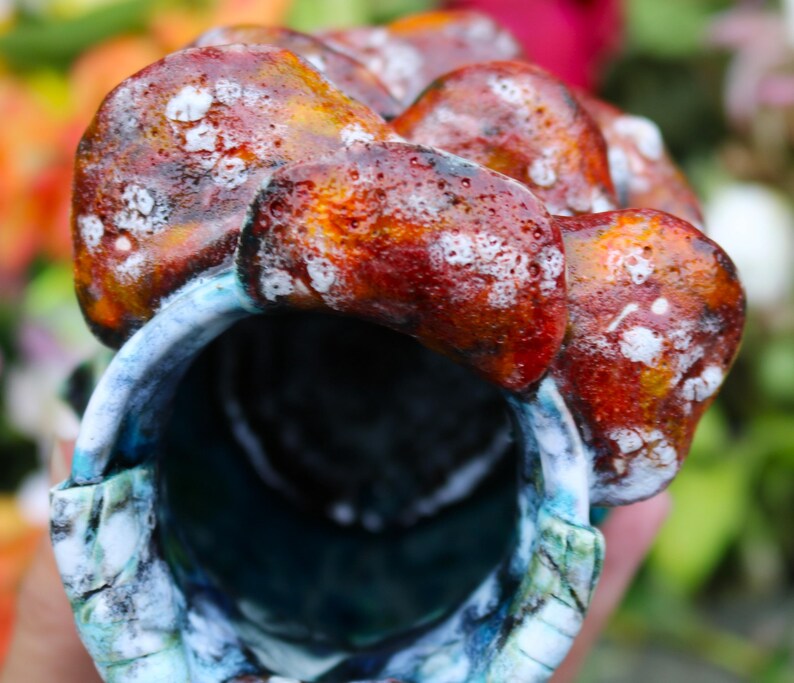 May include: A ceramic vessel with a textured, organic design. The exterior features a blend of reddish-brown and orange hues with white speckles. The interior is a deep blue, with hints of turquoise and white along the rim. The vessel has a unique, artistic appearance.