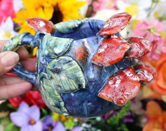 May include: A blue ceramic mug with a handle, decorated with red and white mushrooms and green leaves.