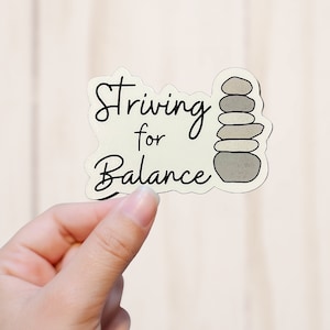 May include: A white sticker with black text that reads "Striving for Balance" and a graphic of a stack of gray stones.