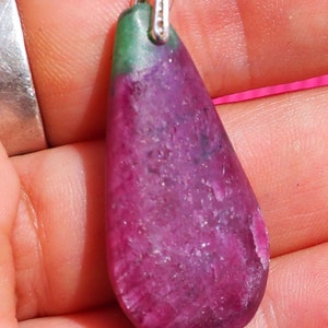 Könnte beinhalten: Ein tropfenförmiger Anhänger mit einer silbernen Öse und einem rosa-grünen Edelstein. Der Edelstein hat eine raue, strukturierte Oberfläche.