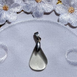 May include: A clear glass teardrop pendant with a silver bail. The pendant is on a white background.