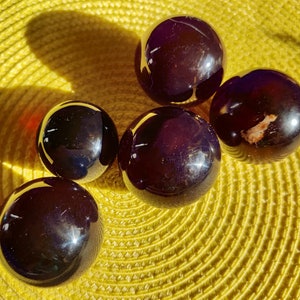 May include: Five smooth, dark purple spheres, likely made of glass or crystal, are arranged on a yellow woven surface. The spheres reflect light, creating a shiny, almost iridescent effect.