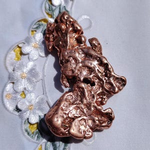 May include: A large, irregularly shaped piece of raw copper with a reddish-brown color. The copper has a rough, textured surface and appears to be naturally formed.