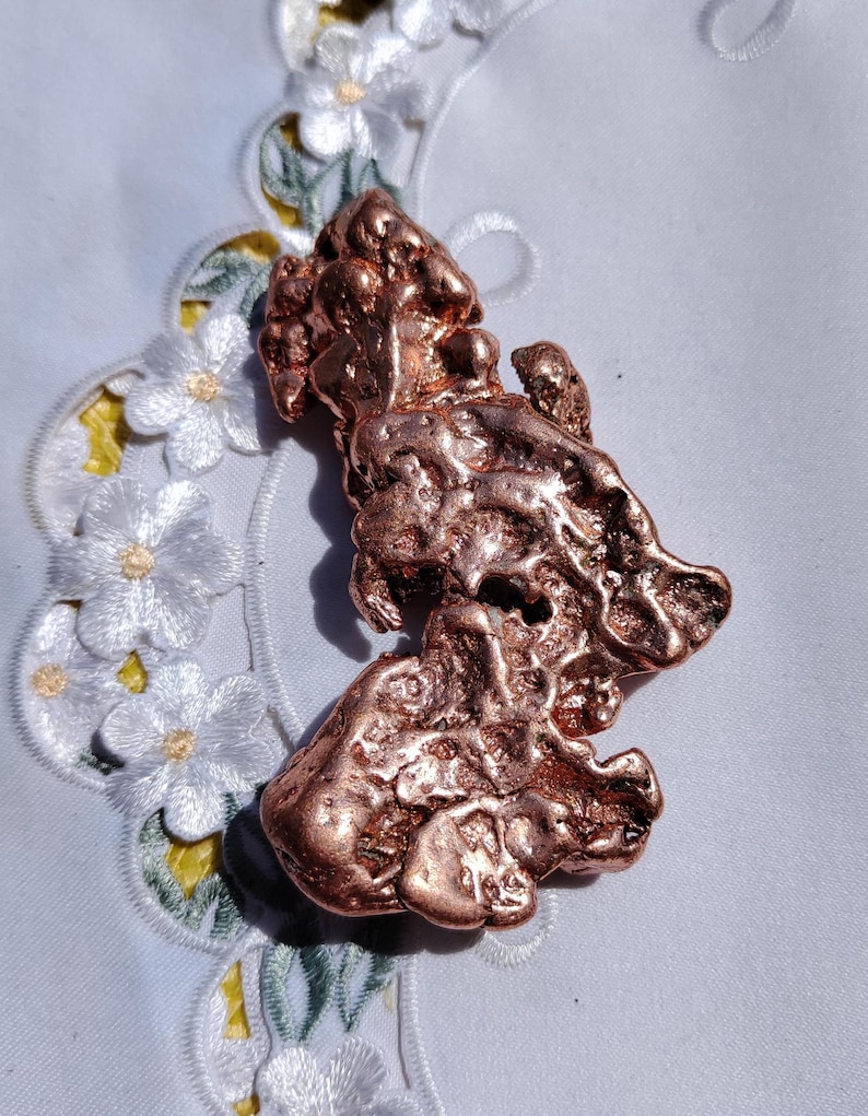 May include: A large, irregularly shaped piece of raw copper with a reddish-brown color. The copper has a rough, textured surface and appears to be naturally formed.