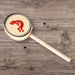 May include: A wooden hand drum with a red and black design on the front. The drum has a long wooden handle and two black beads attached to strings.