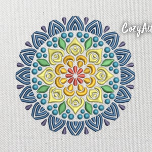 May include: Embroidered mandala design in a circular pattern. The design features a vibrant color palette of blue, green, yellow, orange, and purple. The text "CozyArt" is in the upper right corner. The design is on a white fabric.