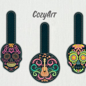 Puede incluir: Tres adornos bordados coloridos con un diseño de calavera con detalles florales. El adorno del medio tiene una guitarra y notas musicales.
