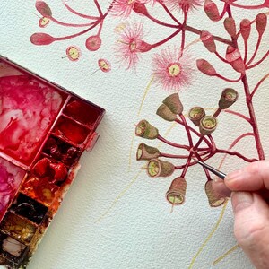 May include: A watercolour painting of a pink flower with green buds. The artist is using a small brush to paint the buds. A watercolour palette with red, orange, and yellow paint is in the bottom left corner of the image.