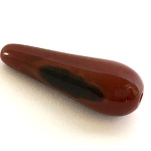 Puede incluir: Una piedra preciosa de ágata roja en forma de lágrima con marcas negras y marrones.