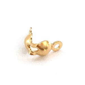 Könnte beinhalten: Ein kleiner, goldfarbener Schmuckverschluss, wahrscheinlich für eine Halskette oder ein Armband. Der Verschluss hat eine abgerundete Form mit einer Schlaufe an einem Ende und einem gebogenen, offenen Abschnitt am anderen. Das Metall hat eine glänzende Oberfläche.