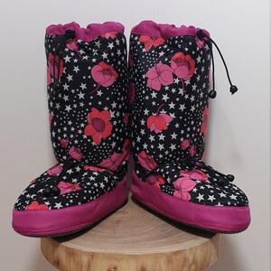 May include: A pair of black and pink fleece boot covers with a floral and star pattern. The boot covers have a drawstring at the top and a pink trim around the bottom.