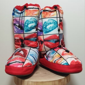 May include: Red and black slipper boots with a colourful print of lips. The boots have a drawstring closure at the top.