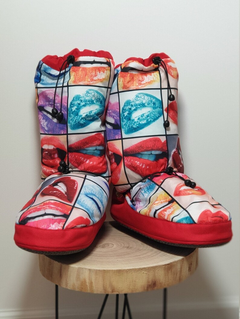 May include: Red and black slipper boots with a colourful print of lips. The boots have a drawstring closure at the top.