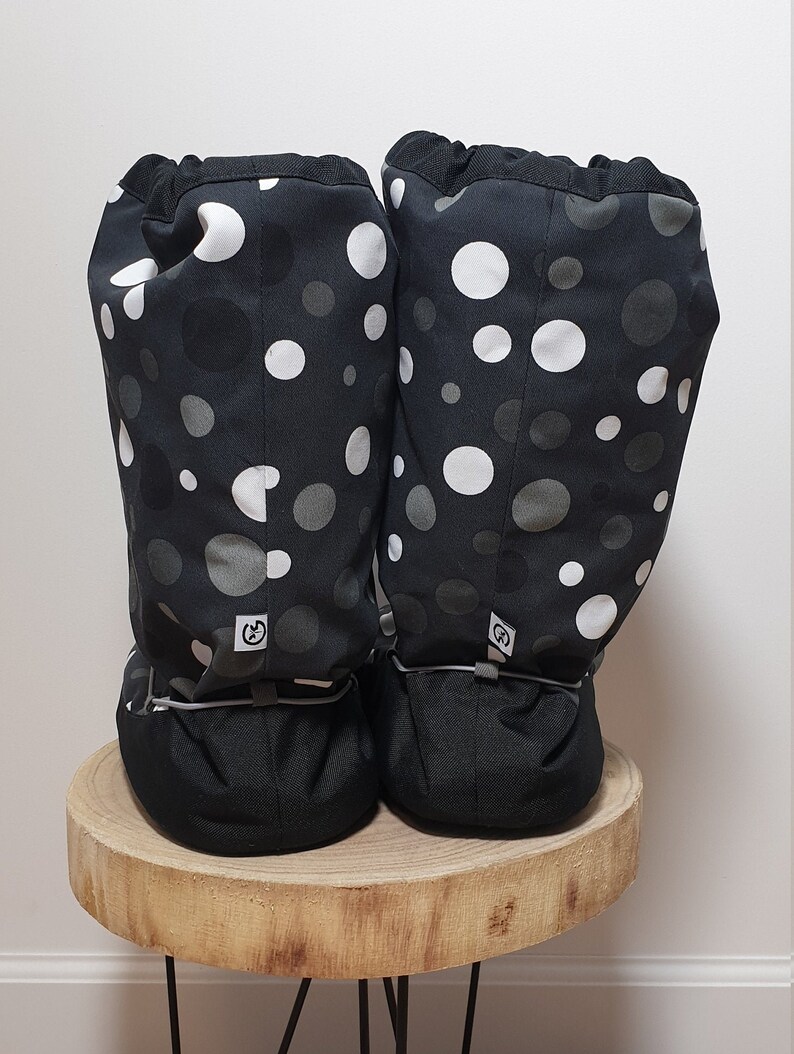 May include: A pair of black fabric boot covers with a white and gray polka dot pattern. The boot covers have a drawstring at the top and a black elastic band at the bottom.