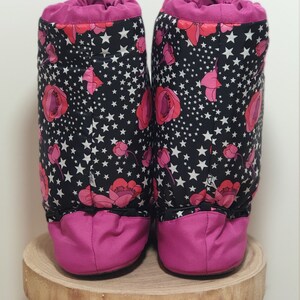 May include: A pair of pink and black fleece boot covers with a floral and star pattern. The boot covers are made of a soft, comfortable material and are perfect for keeping your feet warm in the winter.