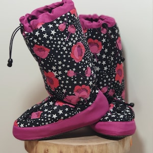 May include: A pair of pink and black fleece lined indoor boots with a drawstring closure. The boots have a floral and star pattern.