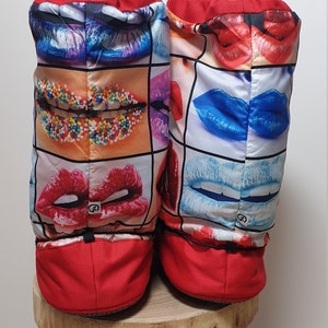 May include: A pair of red slipper boots with a colourful print of lips and sprinkles. The boots have a drawstring at the top and a red bottom.