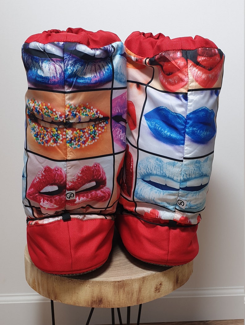 May include: A pair of red slipper boots with a colourful print of lips and sprinkles. The boots have a drawstring at the top and a red bottom.