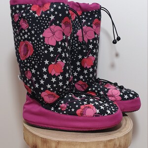 May include: A pair of pink and black fleece boot liners with a floral and star pattern. The boot liners have a drawstring closure at the top.