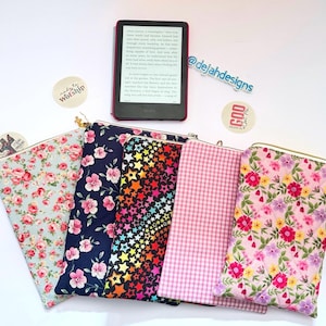 May include: Several fabric pouches with diverse patterns, such as floral, star, and gingham. An e-reader is displayed on top. The pouches have gold-coloured zippers. The background includes stickers with text.